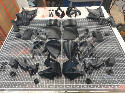 A variety of black 3D-printed parts for the Midnight Rulers Helmet are arranged neatly on a cutting mat grid, including detailed segments—crafted from digital download 3D print files and ready for assembly.