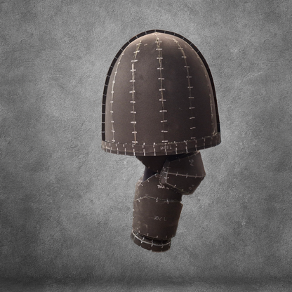 A helmet-shaped sculpture featuring the stitched, patchwork design of the V.10 Tactical Arms Pattern, inspired by Galactic Warriors arms and crafted from a dark material, floats against a textured gray background.