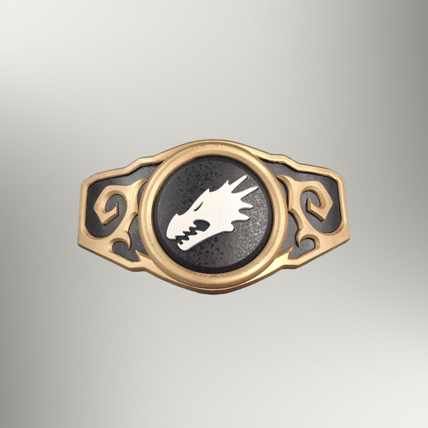 A gold-toned metal belt buckle featuring a central circular black insert with a white dragon head emblem, flanked by ornate scrollwork on a light gray gradient background.