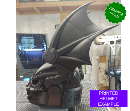 A striking black Midnight Rulers Helmet (3D Print | Files Only), featuring large bat wings on each side, rests on a workshop table. On-screen text displays “EXAMPLE BUILD” and “PRINTED HELMET EXAMPLE.” 3D printers and shelves in the background showcase that this impressive creation was made using downloadable files for the Midnight Rulers Helmet (3D Print | Files Only).