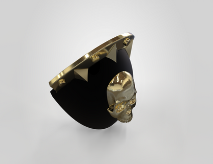 A black, curved object with a shiny gold skull at its center and gold pyramid studs lining the top edge, set against a plain light background. This eye-catching piece is the V.10 Knee Skull Detail V.1 (3D Print | Files Only), designed as a 3D printable knee accessory ideal for collectors and cosplay enthusiasts.