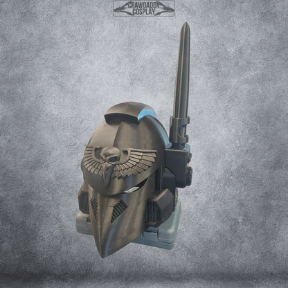A sleek black V.7 Eagle - Sable Sentry Helmet (3D Print | Files Only) with a futuristic design, featuring a prominent bird and wing emblem, long crest spike, and silver visor rests on a textured stone-gray background. Ideal for cosplay enthusiasts, this digital download provides detailed 3D print files. The Crawdad Cosplay logo is subtly visible at the top.