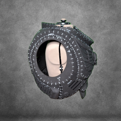 A mannequin head is placed inside a large, hollow black tire with white markings, set against a gray textured background, evoking the futuristic aesthetics of the V.10 Tactical Chest Pattern—perfect as inspiration for your next EVA foam template or digital download project.