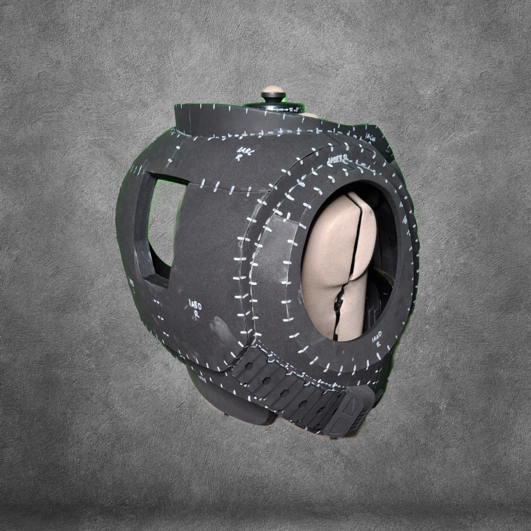 A spherical, black object with stitched seams and a beige interior sits against a gray textured background. Designed with large openings and reminiscent of Galactic Warriors’ armor, this structure is the V.10 Tactical Chest Pattern—a stylized, padded helmet or mask ideal for use as an EVA foam template or digital download for cosplay projects.