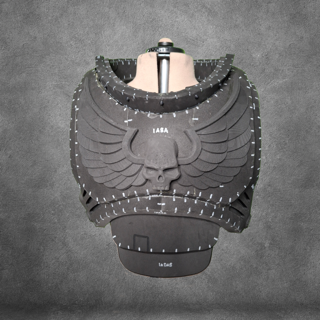 Introducing the V.10 Tactical Chest Pattern: a black armored chestplate featuring an intricate skull and wings motif, showcased on a mannequin against a gray textured background. Detailed with white markings and numbers across the armor plates, this design is ideal as an EVA foam template for constructing your own Galactic Warriors chest armor. Instantly accessible as a digital download for your convenience.