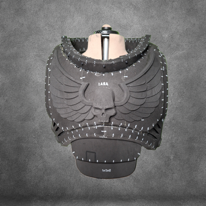 Introducing the V.10 Tactical Chest Pattern: a black armored chestplate featuring an intricate skull and wings motif, showcased on a mannequin against a gray textured background. Detailed with white markings and numbers across the armor plates, this design is ideal as an EVA foam template for constructing your own Galactic Warriors chest armor. Instantly accessible as a digital download for your convenience.
