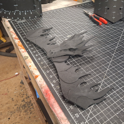 A 3D-printed black dragon head and wings—featuring intricate details from the V.10 Fire Lizards Chest Detail (3D Print | Files Only)—rest on a cutting mat, with tools and crafting materials visible in the background.