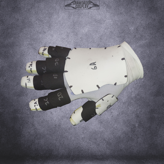 A white glove with black marked segments on each finger and handwritten labels is displayed on a textured gray surface. Inspired by the iconic Galactic Warriors Universal Gloves, this piece highlights visible seam lines and serves as the perfect EVA foam template for cosplay or costume creation. The “Galactic Warriors Universal Glove Pattern” is offered as a digital download reference, ideal for crafting your own interstellar costume accessories.