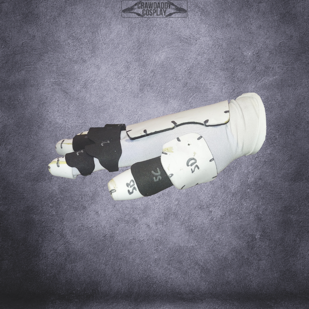 A white and black robotic glove or bracer with numbered sections, modeled for cosplay and displayed against a textured gray background. This design is based on the Galactic Warriors Universal Glove Pattern and is offered as a digital EVA foam template download for easy crafting.