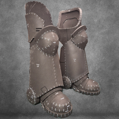 Two unfinished foam armor greaves and sabatons with visible seams, white markings, and stitches—crafted using the V.10 Tactical Legs Pattern for EVA foam—stand upright against a textured gray background. Perfect for cosplay projects, this detailed digital download offers everything needed to create Galactic Warriors-style leg armor.