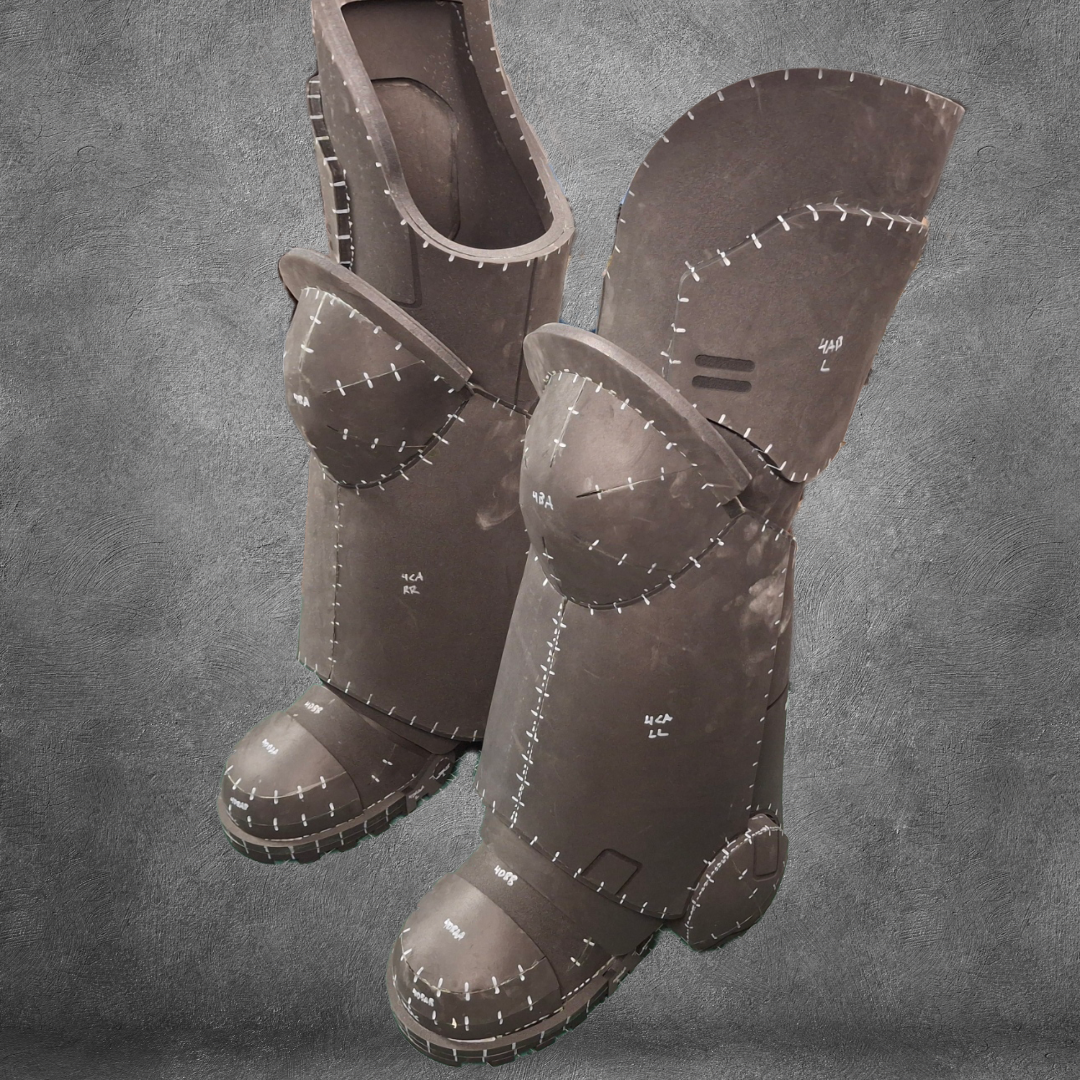 Two large, brown, foam costume boots featuring exaggerated stitched seams and armor-inspired panels—perfect for finishing your Galactic Warriors legs—stand upright against a textured gray background. The V.10 Tactical Legs Pattern EVA foam template is available as a convenient digital download.