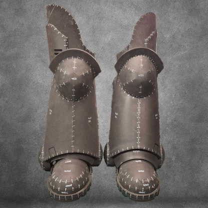 A pair of V.10 Tactical Legs Pattern black metal greaves featuring white markings and measurement lines, inspired by Galactic Warriors legs, displayed against a gray textured background.