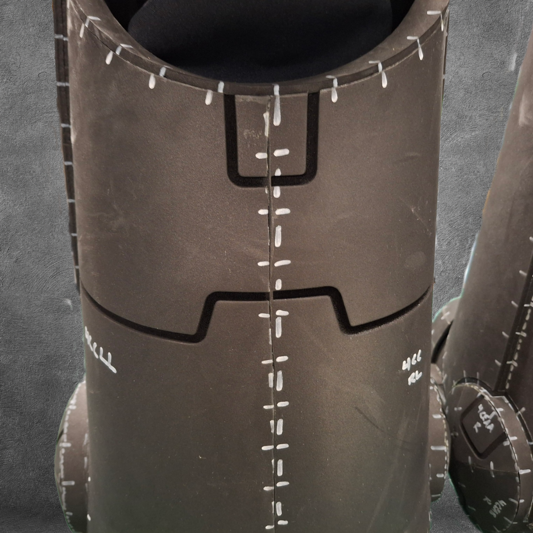 Close-up of the V.10 Tactical Legs Pattern in matte black, featuring white markings and lines reminiscent of stitches or measurements, set against a textured gray background. The form suggests it’s part of a costume or prop—perfect for digital download enthusiasts crafting sci-fi cosplay legs from this EVA foam template inspired by Galactic Warriors.