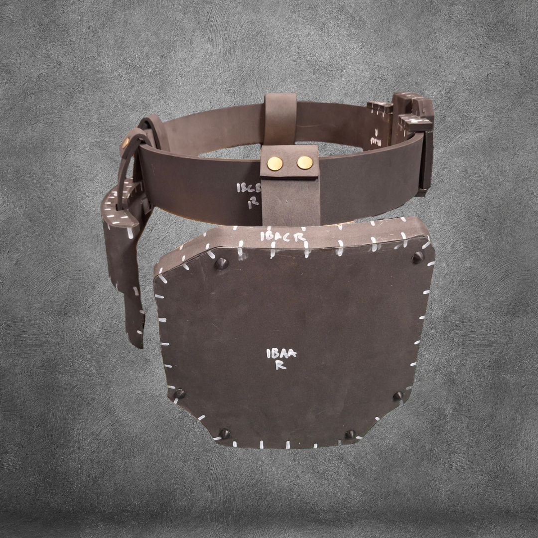 A brown, rectangular piece of armor with white markings and stitching, attached to a matching belt, is displayed against a textured gray background—perfect for fans seeking the V.10 Tactical Waist Pattern EVA foam template as a digital download.