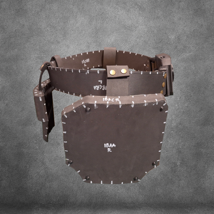 A brown V.10 Tactical Waist Pattern belt with a large, rectangular leather guard attached—styled in a Galactic Warriors fashion—is displayed against a gray textured background. White markings and visible stitching adorn the belt and guard. Ideal for cosplay or crafting, this EVA foam template is available as a digital download.