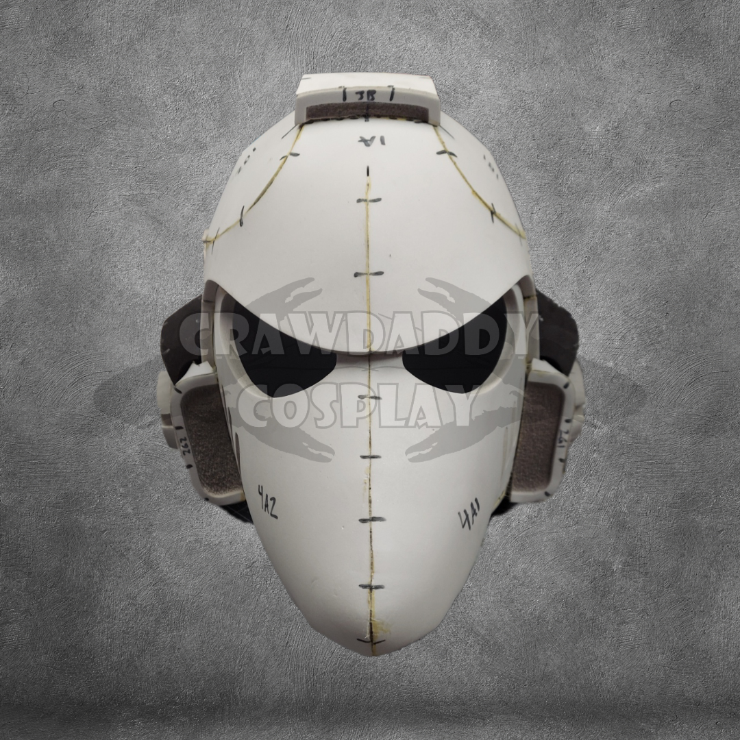 The Galactic Warriors Universal Beaked Helmet Pattern is displayed against a textured gray background. With its white, futuristic design featuring black visor slits, stitching-like lines, and headphone-like ear coverings, this pattern is perfect for cosplay enthusiasts and also serves as excellent inspiration for an EVA foam helmet template or digital download project.