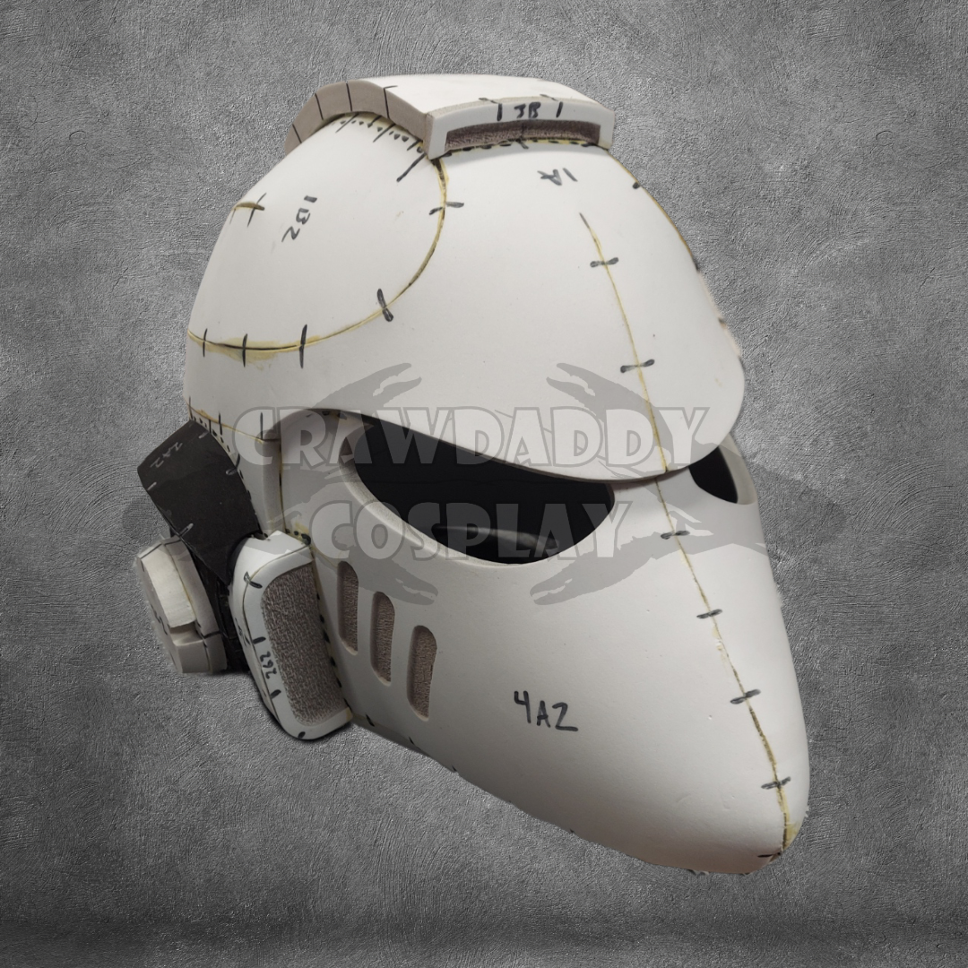 A white sci-fi or futuristic helmet, featuring visible seams, black eye slits, and text markings reminiscent of a Galactic Warriors Universal Beaked Helmet Pattern. The background is a gray textured surface with a CRAWDADDY COSPLAY watermark across the center.