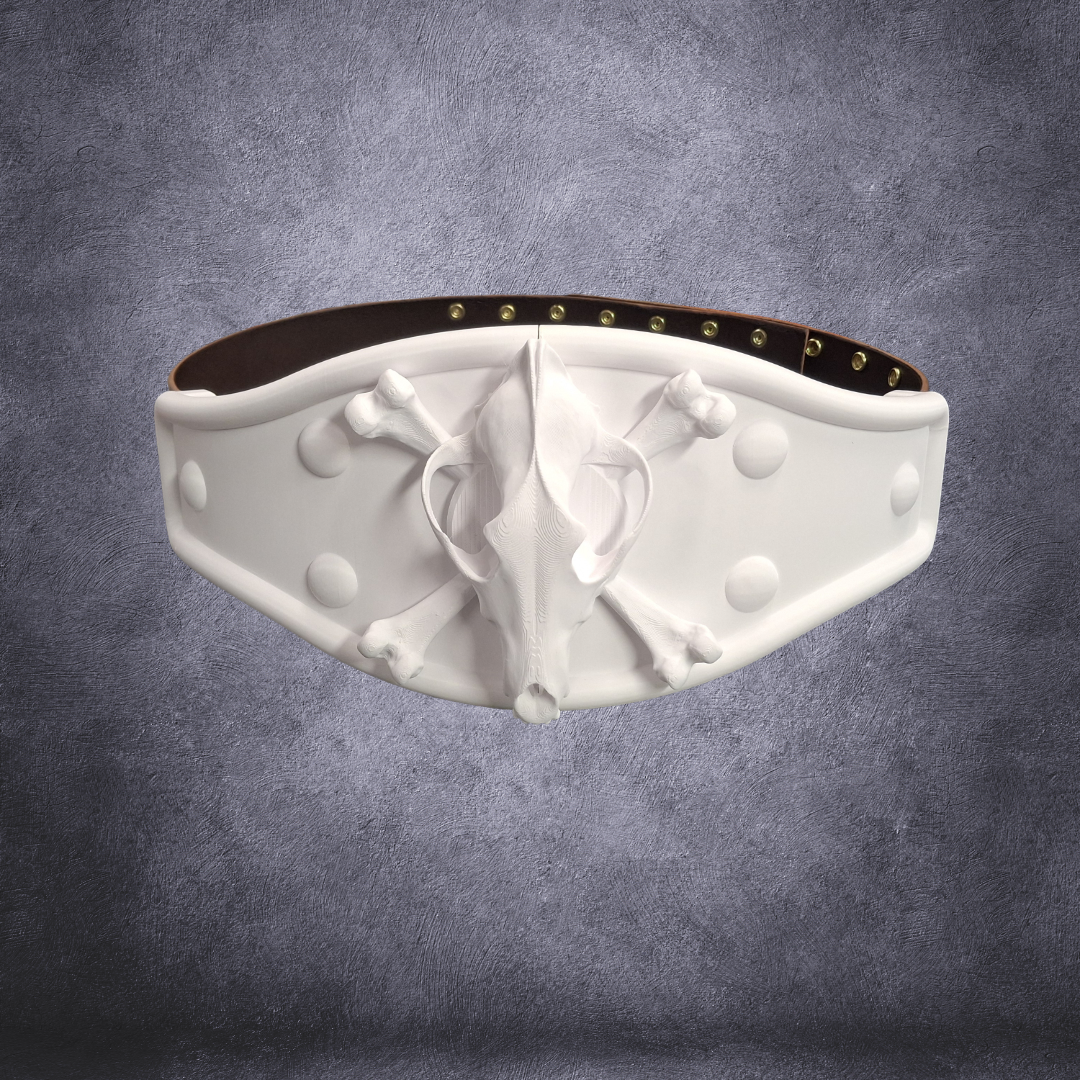A white faux-fur belt featuring a sculpted skull and crossbones motif in the center, flanked by decorative studs, shown against a textured gray background.