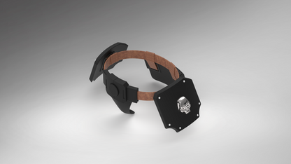 A futuristic black head-mounted display or headset with a brown strap, shown on a clean gray gradient background. The front panel features a silver metallic skull emblem.